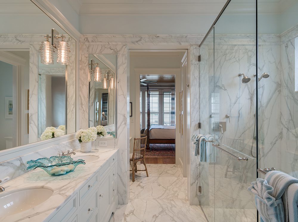 A bathroom with marble counter tops and white cabinets.