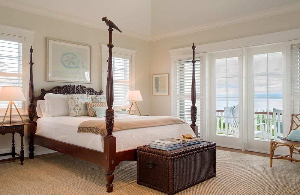 A bedroom with four poster bed and large window.